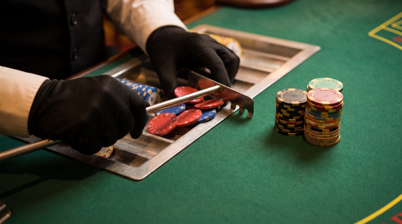 Poker chips being pulled into a rake tray beside reward chips at a live table